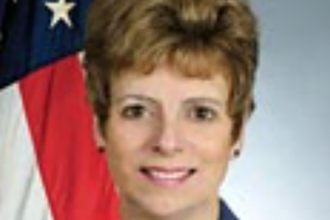 Portrait photo of Mary Glackin beside the flag of United States of America 