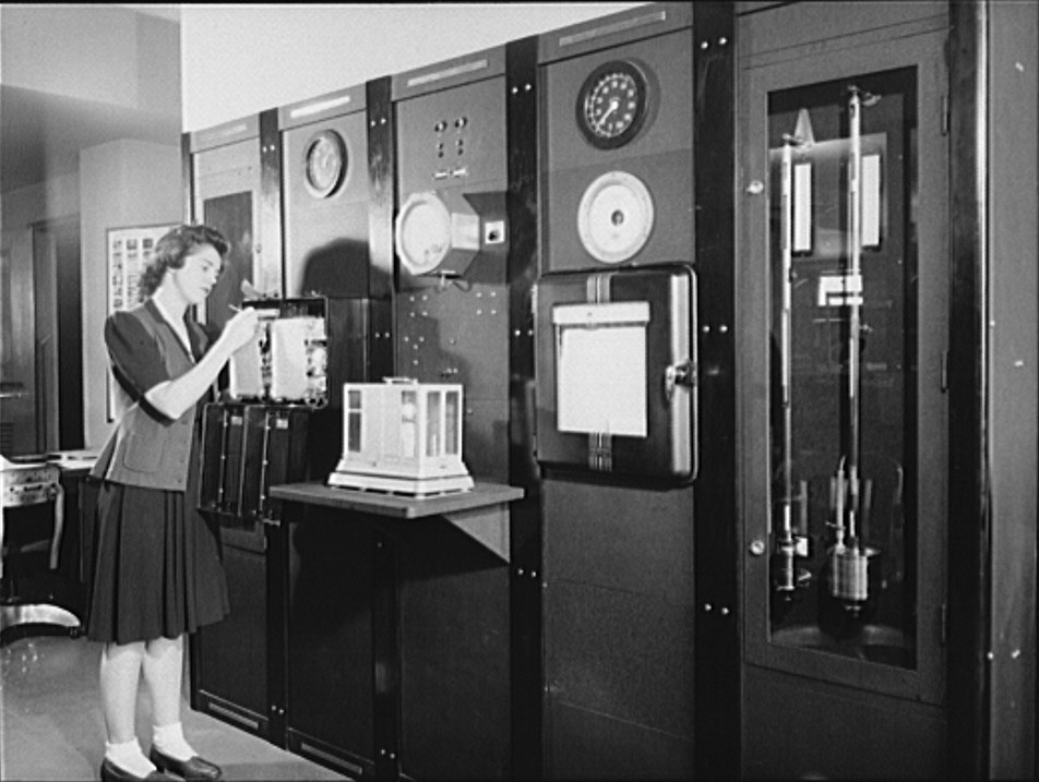 A woman in the Weather Bureau station at National Airport (Washington, DC) is gathering surface weather observations at a Weather Bureau instrument panel on which are mounted barometers, thermometers, wind direction and velocity indicators, and other instruments for measuring weather elements, circa 1943.